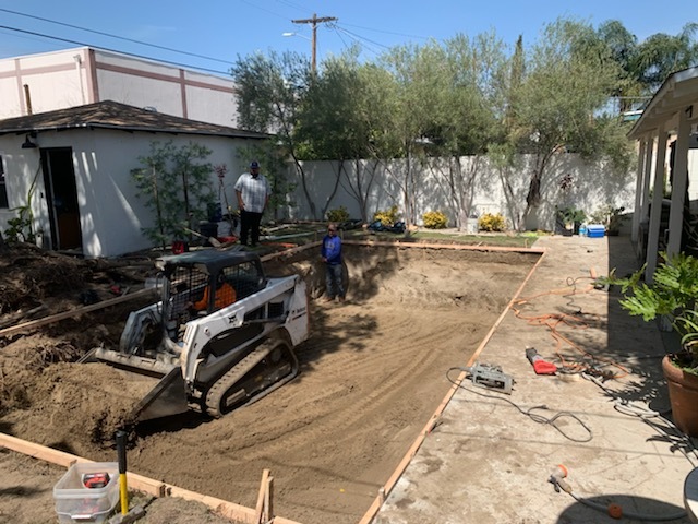 A digger moving dirt for a pool body.