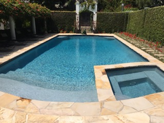 A pool and jacuzzi surrounded by hedges.