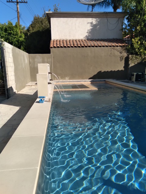 Pool with a corner jacuzzi and water faucets.