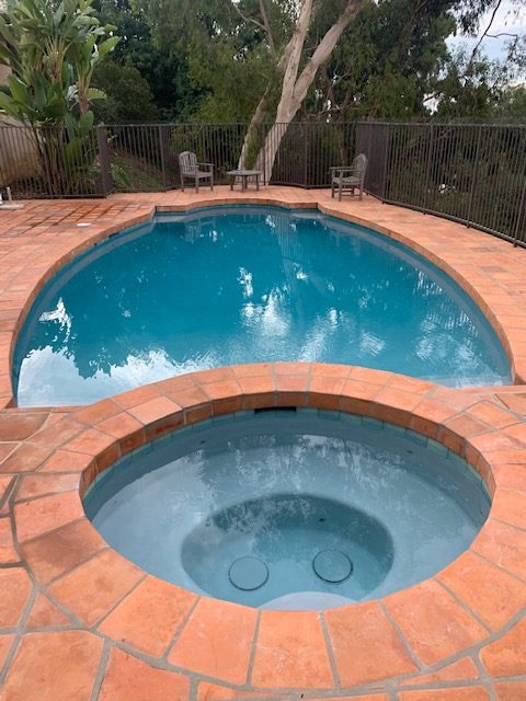 A pool with a smaller jacuzzi under it surrounded by brick.